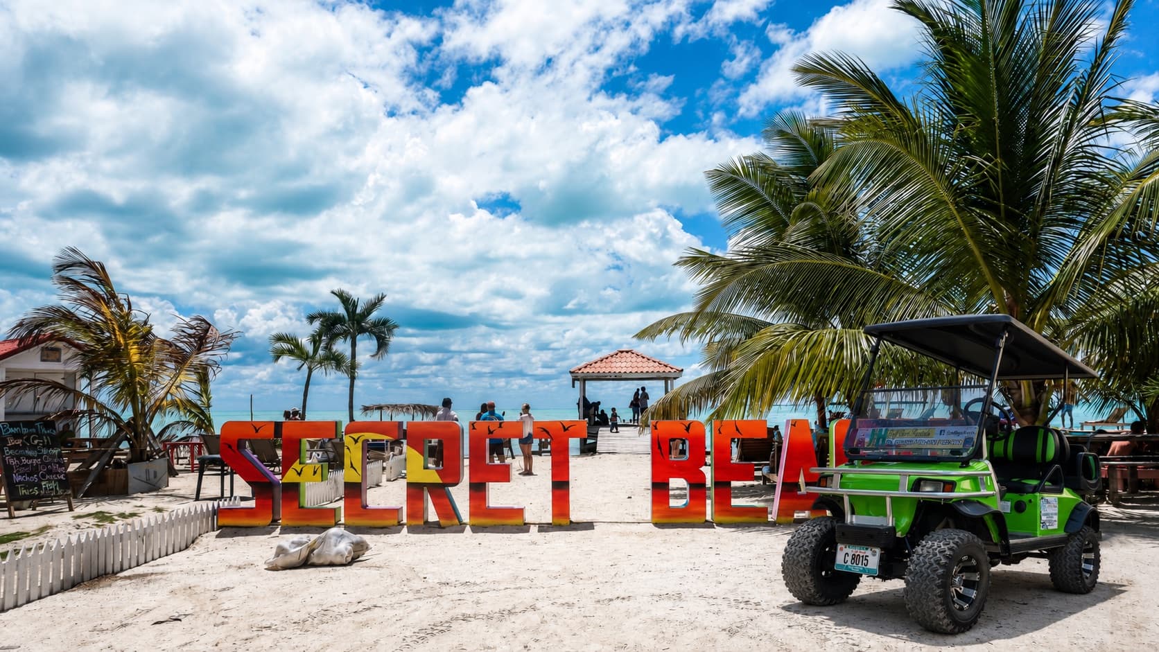 A green J&H rental golf cart parked beside the Secret Beach sign on Ambergris Caye, Belize